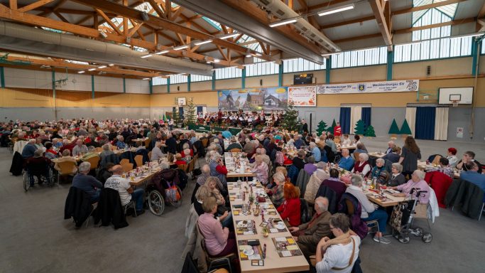 Volles Sportzentrum mit vielen Menschen, die an Tischen sitzend essen und feiern.